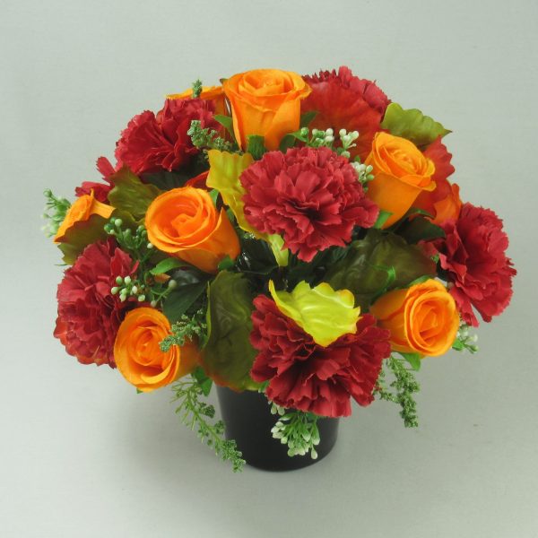 Grave flower arrangement with red large carnations and orange rose buds.